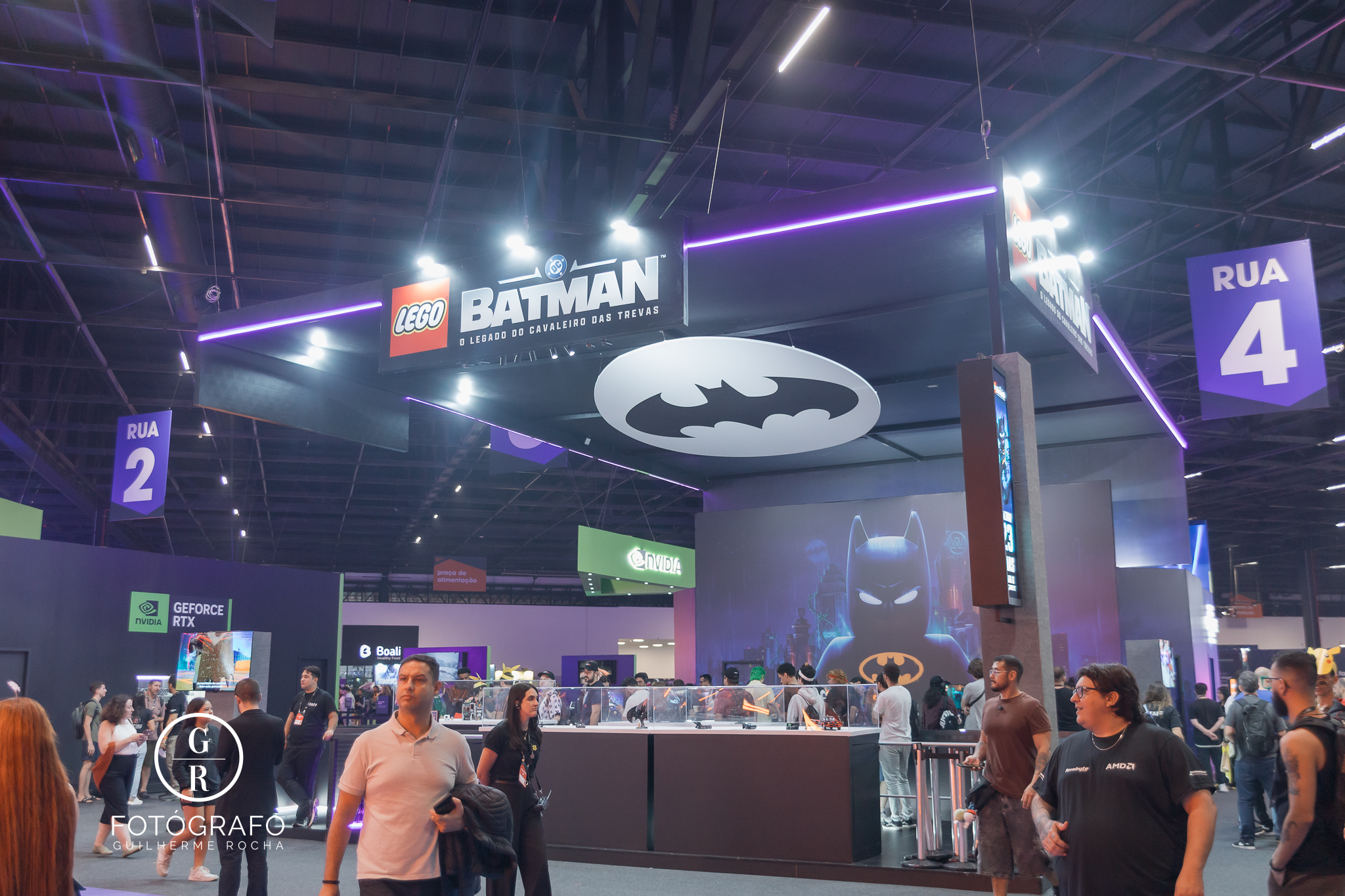 Estande da Warner Bros na gamescom com exposição temática de lego Batman, área interativa e grande logo do herói no teto