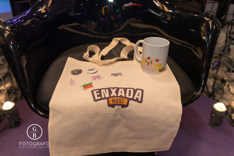Brindes da Enxada com ecobag personalizada, caneca e adesivos distribuídos no estande durante o evento.
