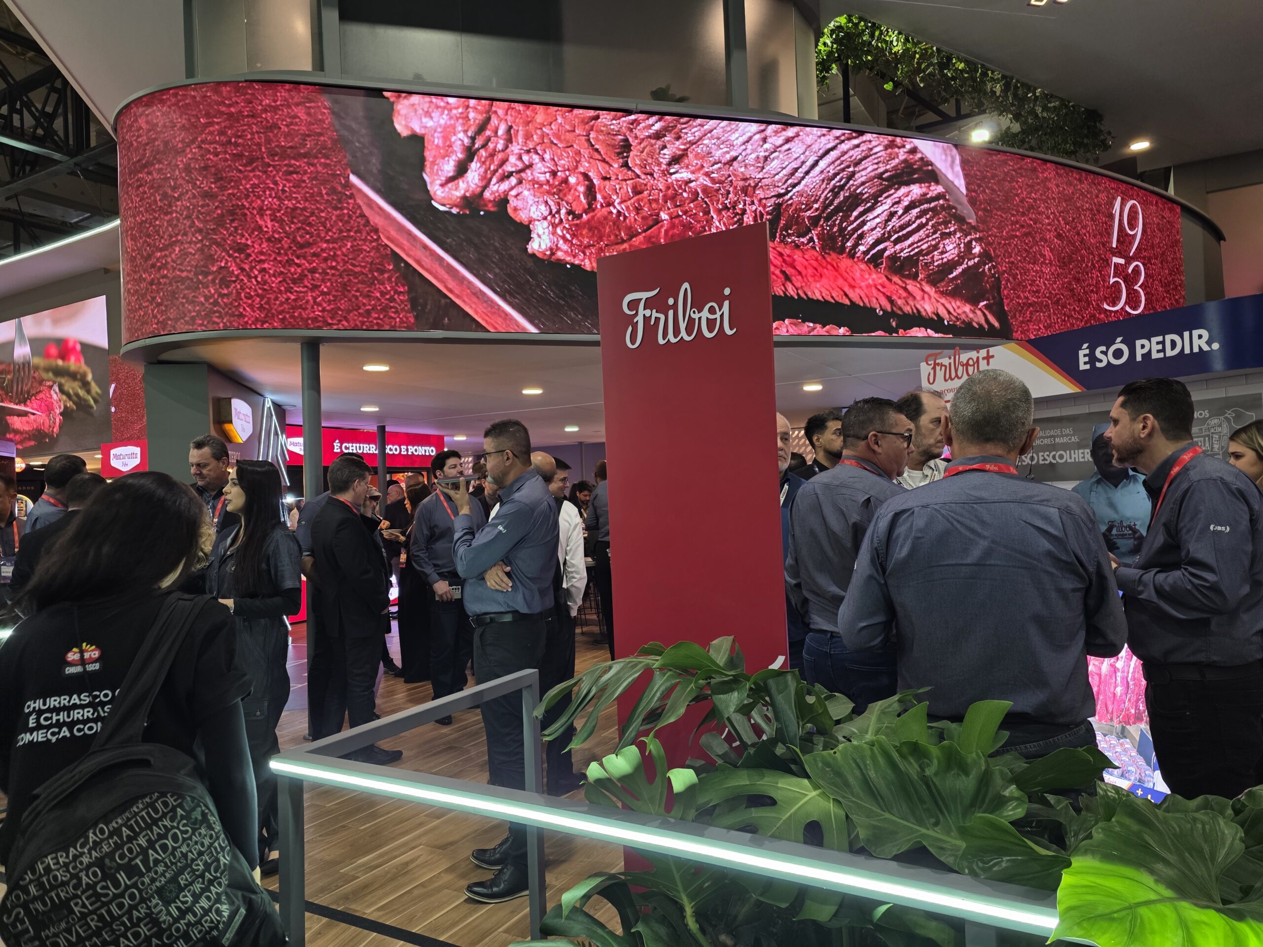 Estande da Friboi durante a APAS Show 2026 com telão exibindo cortes de carne bovina, profissionais reunidos para networking e apresentação das soluções da marca para o varejo alimentar.