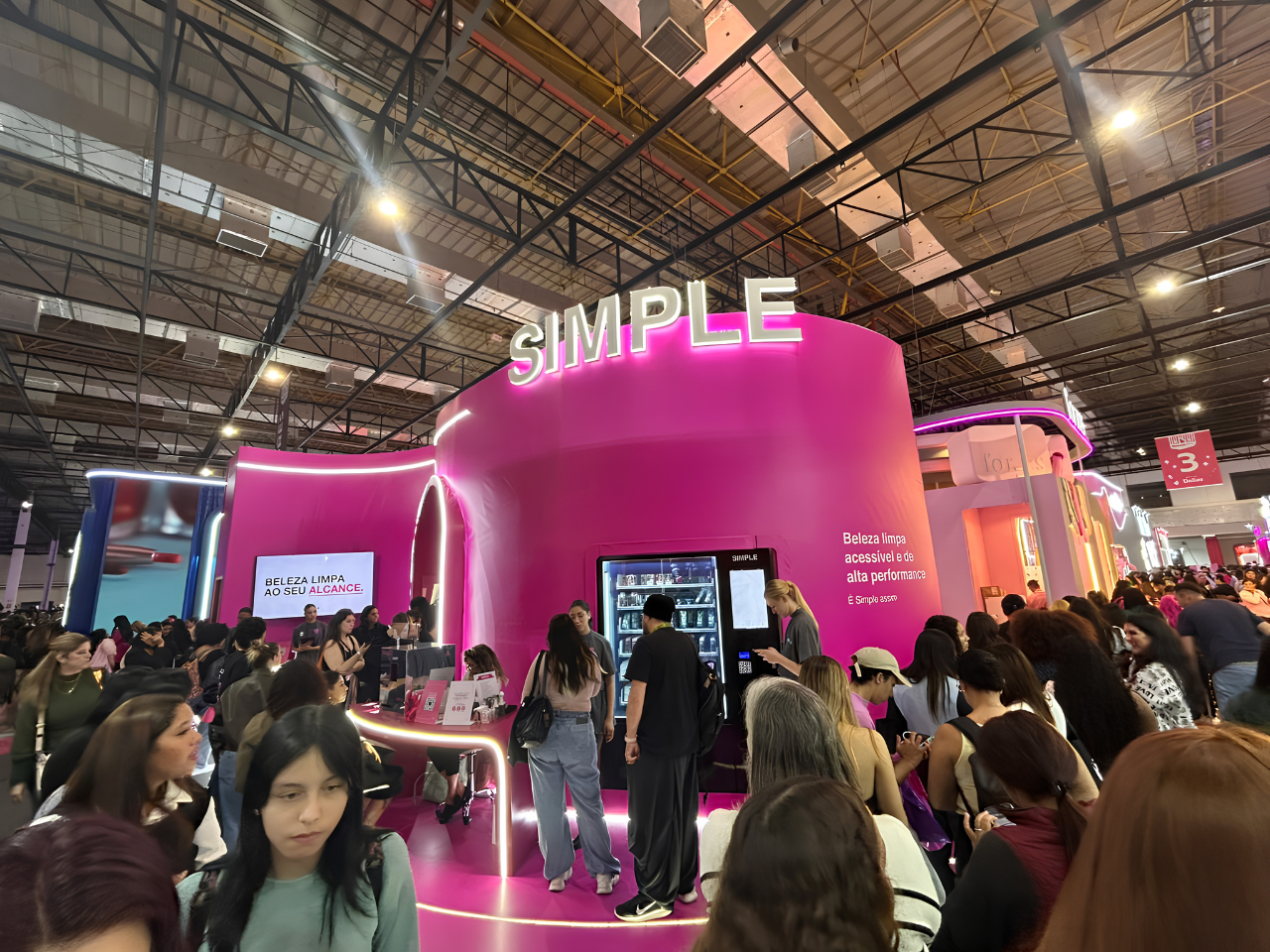 Estande da Simple Organic na Beauty Show 2026 reúne grande público em torno da estrutura rosa em formato de "S", destacando o reposicionamento da marca, a beleza limpa e as ativações interativas para os visitantes.