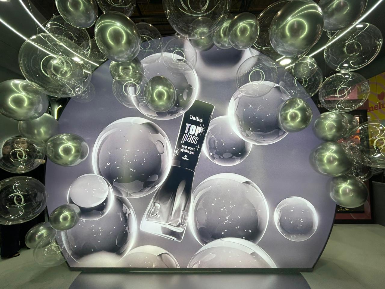 Painel gigante do Dailus Top Glass na Beauty Show 2026, cercado por balões transparentes que remetem ao efeito glossy e ao brilho intenso do top coat efeito gel da marca.