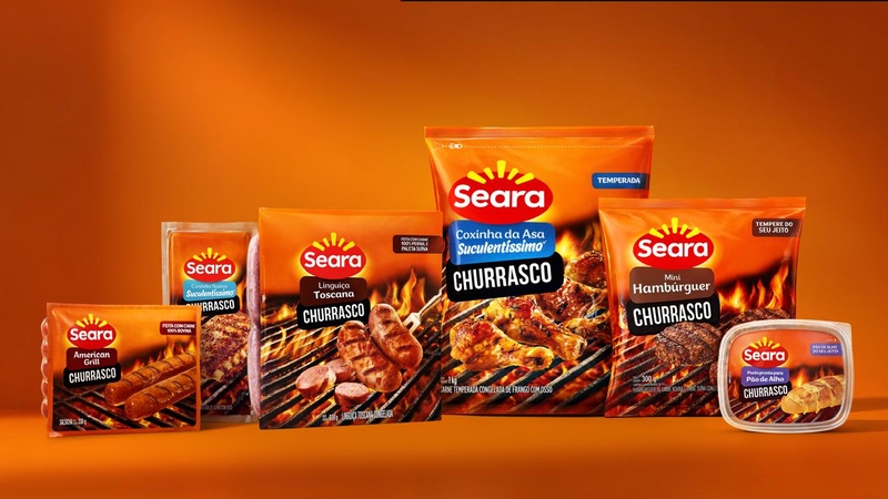 Seara apresenta novos produtos da linha churrasco em embalagem promocional durante divulgação da APAS Show 2026, com linguiças, hambúrgueres, coxinha da asa e pasta de alho sobre fundo alaranjado.