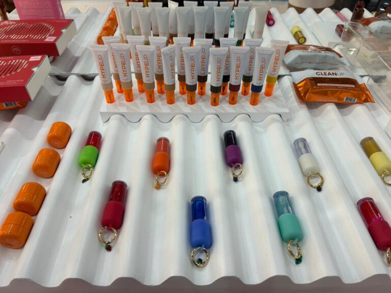 Exposição de produtos da Mari Maria Makeup destaca a linha Hype Up, itens multifuncionais e acessórios coloridos apresentados na feira.