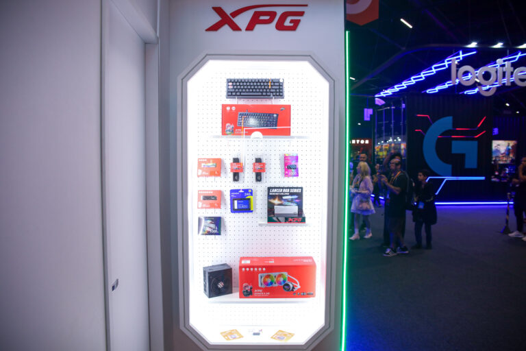 **Texto alternativo (alt text):** Vitrine iluminada da **XPG** na gamescom exibindo periféricos, SSDs, memórias e fonte de energia organizados para demonstração do portfólio gamer da marca.