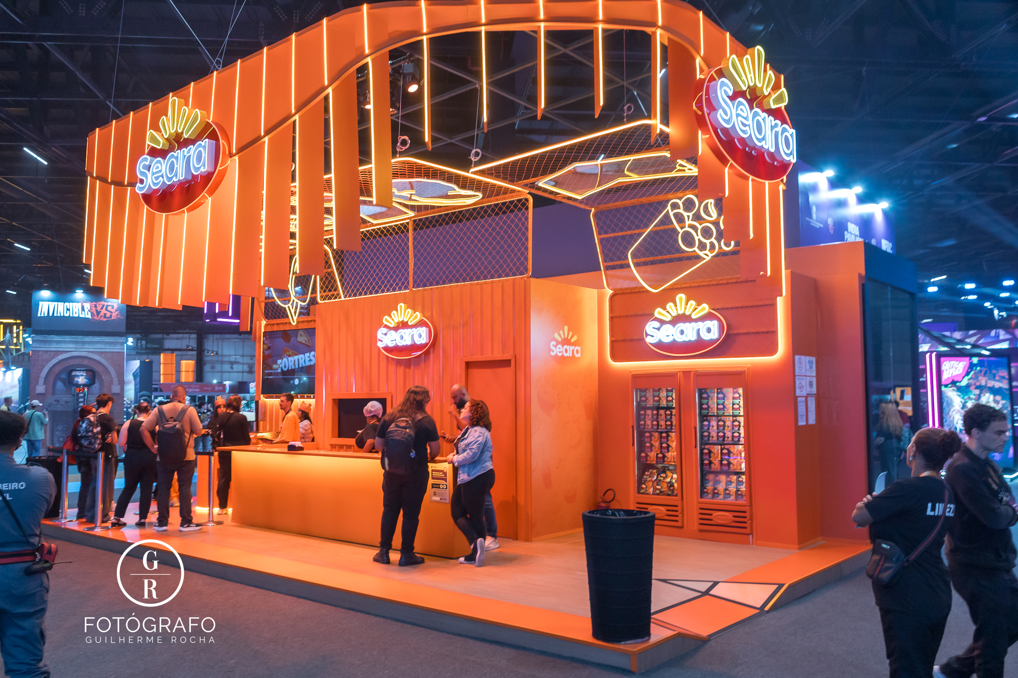 Estande da Seara na gamescom latam com iluminação laranja, área de atendimento e espaço para compra e consumo de produtos.