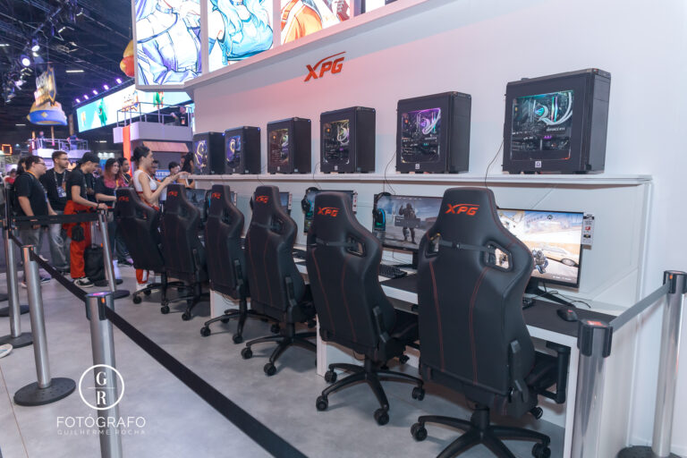 Área de free play da XPG na gamescom com várias estações gamer, cadeiras ergonômicas e visitantes jogando em PCs de alto desempenho.