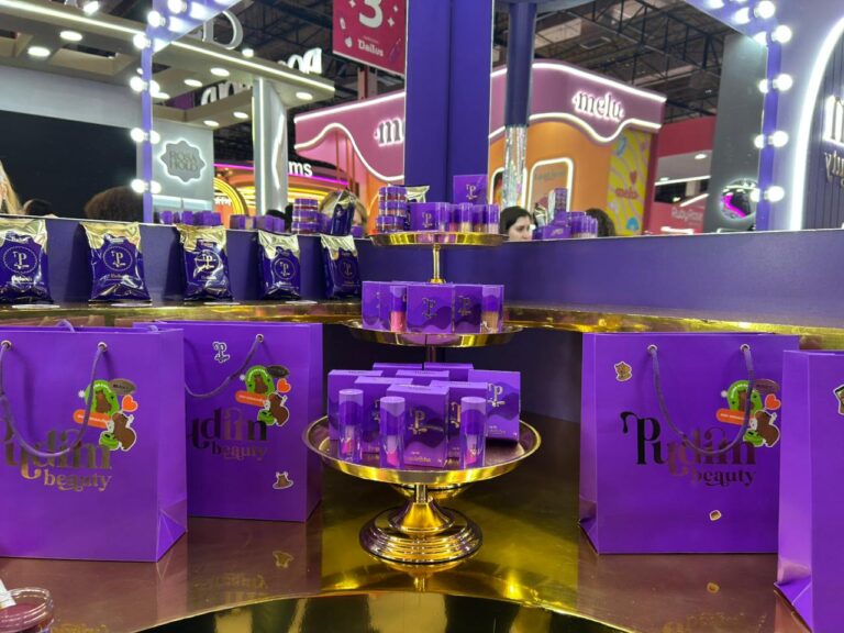 Produtos da Pudim Beauty expostos em área de destaque do estande, com embalagens roxas personalizadas, linha de maquiagens veganas e decoração inspirada no universo da marca.