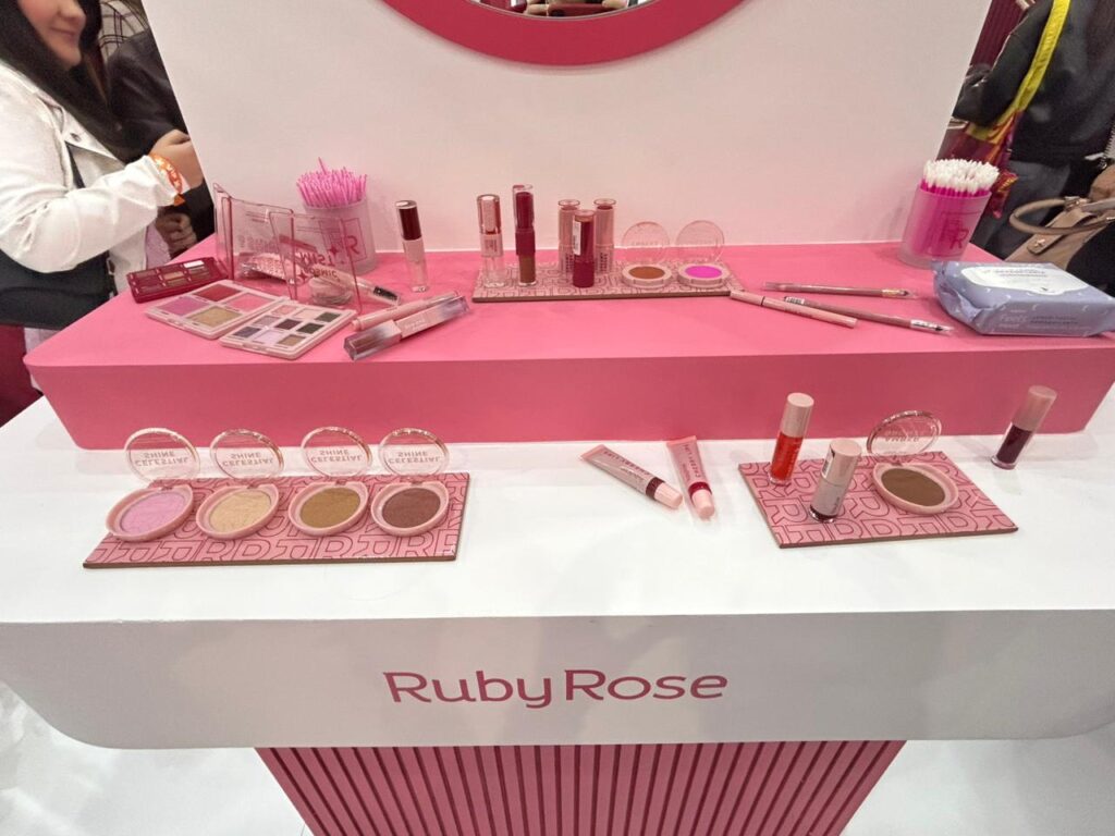 Bancada de maquiagem da Ruby Rose exibe paletas, iluminadores, produtos labiais e itens para teste, permitindo que visitantes conheçam os lançamentos da marca.