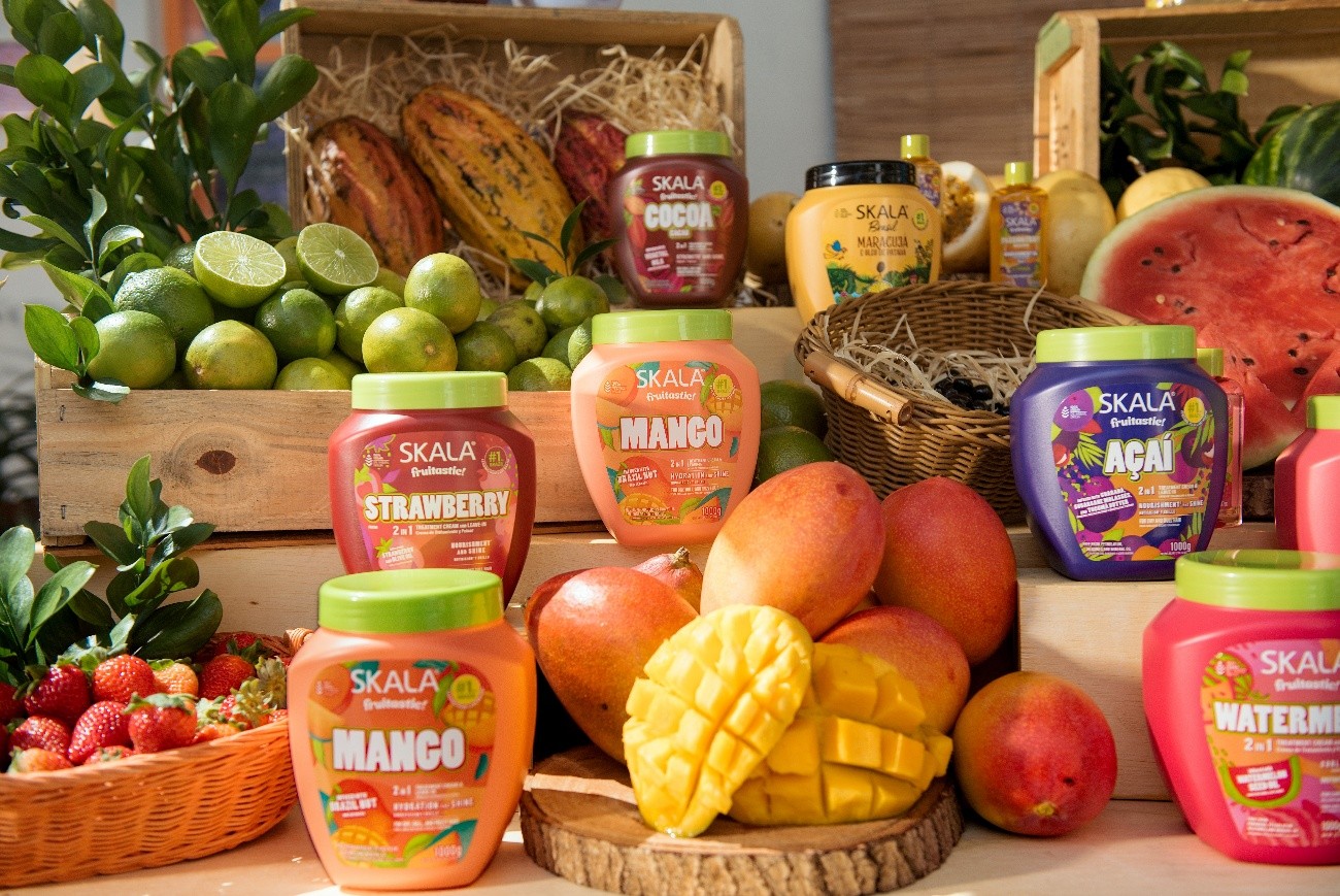 Linha Fruitastic da Skala exposta entre frutas frescas, incluindo manga, morango, açaí e melancia, reforçando a inspiração tropical e vibrante da marca.