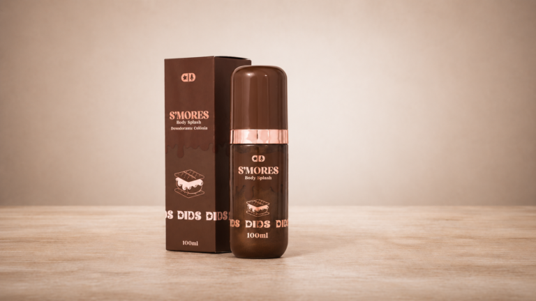 Dids Body Splash S'Mores em embalagem marrom com detalhes rosé gold e partículas iluminadoras visíveis no frasco. O produto está posicionado ao lado da caixa da coleção em cenário minimalista.