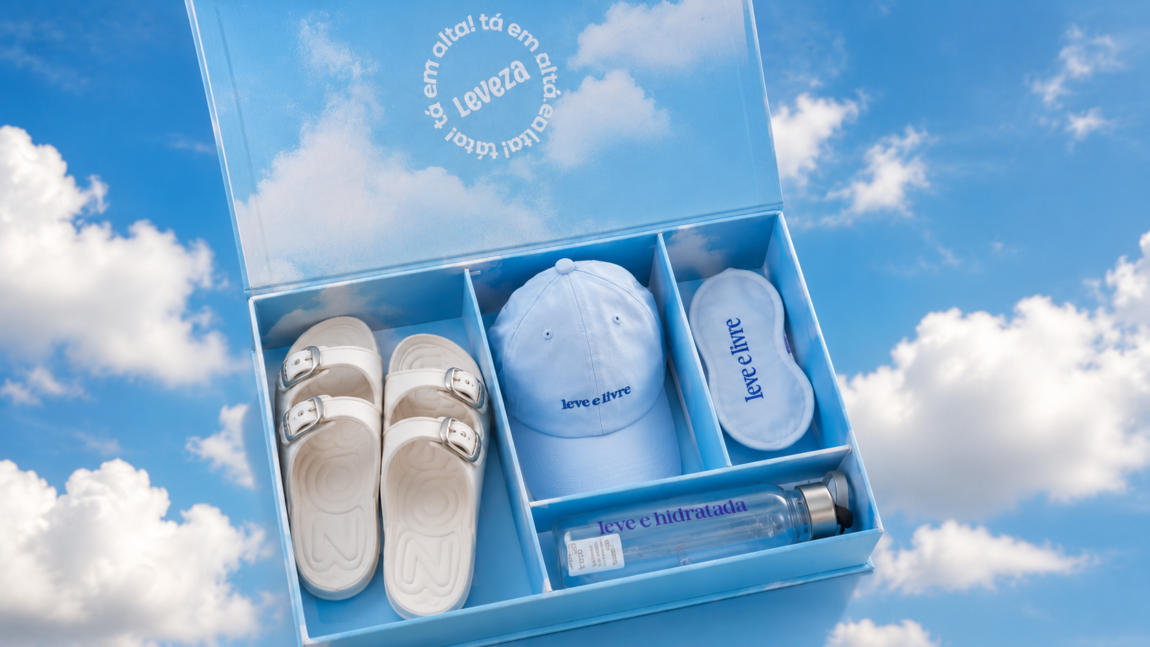 Kit recebido da Zaxy com sandália branca, boné, máscara de descanso e garrafa em caixa personalizada sobre fundo de céu azul com nuvens.