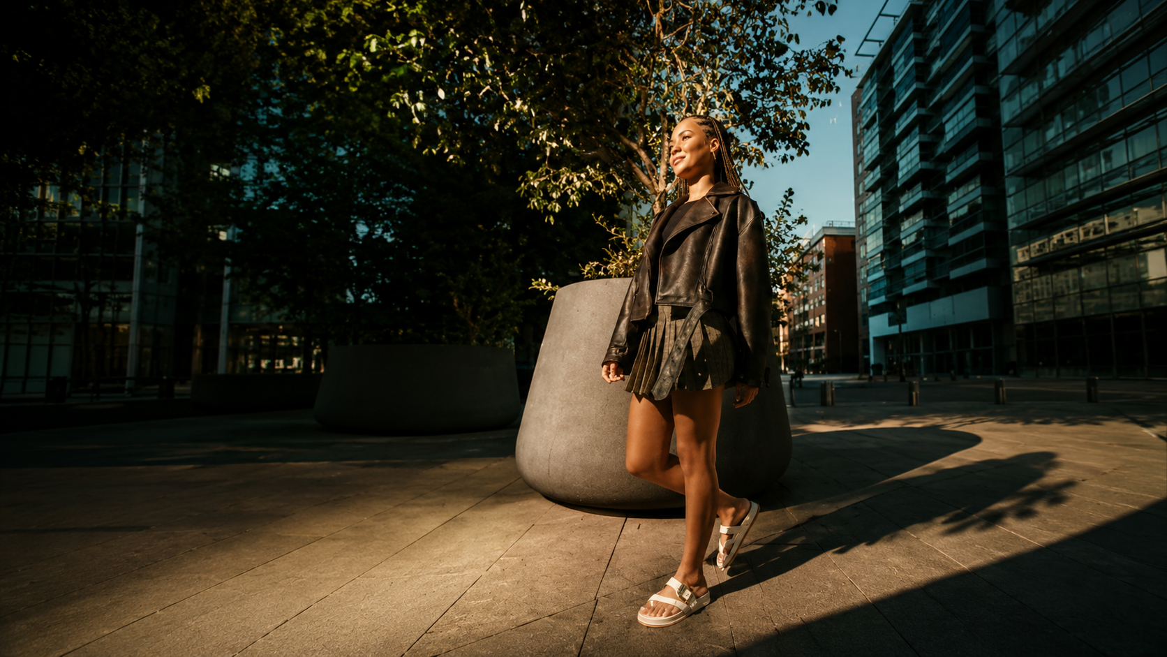 Modelo usa sandália Zaxy em produção de outono-inverno com jaqueta de couro e saia plissada, mostrando a versatilidade do calçado em diferentes estações.