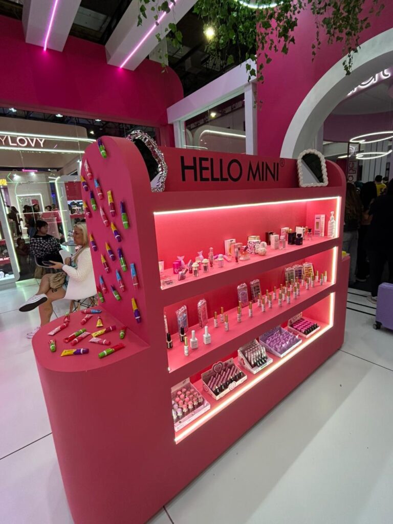 Mostruário da Hello Mini reúne maquiagens, glosses, cuidados para unhas e produtos de beleza em estande iluminado durante a Beauty Show 2026.