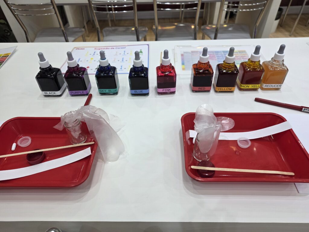 Mesa interativa da Pentel apresenta tintas e materiais utilizados na criação personalizada de cores de canetas durante a feira.