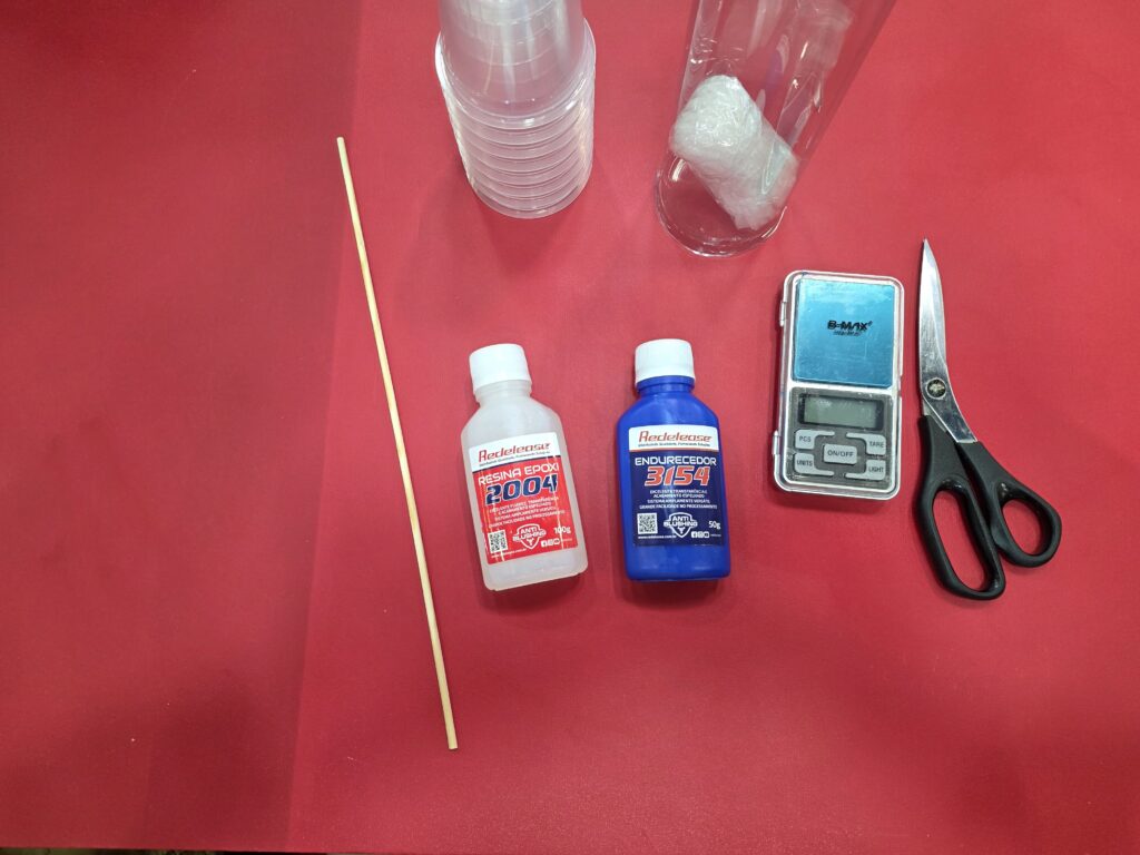 Materiais utilizados nas aulas da Redelease incluem resina epóxi, endurecedor, balança de precisão e utensílios para mistura e aplicação.