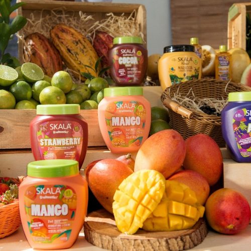 Linha Fruitastic da Skala exposta entre frutas frescas, incluindo manga, morango, açaí e melancia, reforçando a inspiração tropical e vibrante da marca.