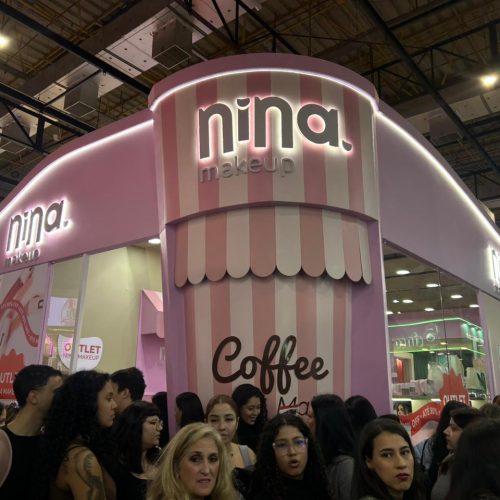 Estande da Nina Make Up na Beauty Show 2026 com fachada inspirada em cafeteria, identidade visual rosa e destaque para a linha Coffee Make, atraindo visitantes durante o evento.