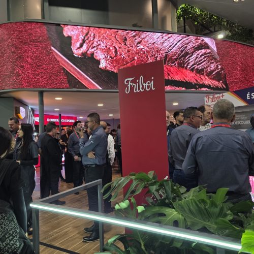 Estande da Friboi durante a APAS Show 2026 com telão exibindo cortes de carne bovina, profissionais reunidos para networking e apresentação das soluções da marca para o varejo alimentar.