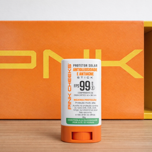 Protetor solar stick FPS 99 da Pink Cheeks antioleosidade e antiacne, em destaque com embalagem branca e laranja, posicionado à frente da caixa do produto.