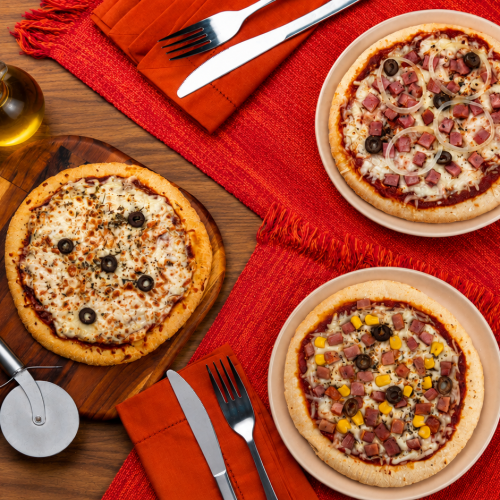 Pizzas congeladas Seara em mesa de madeira com três sabores, azeite e utensílios de cozinha.
