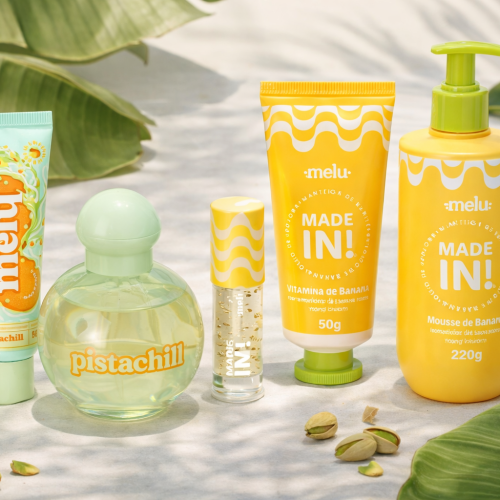 Linha melu Made In e Pistachill com hidratantes, lip oil, desodorante colônia e mousse de banana, dispostos sobre superfície clara com folhas tropicais, bananas e pistaches decorativos ao redor.
