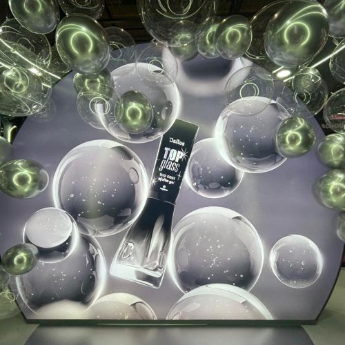 Painel gigante do Dailus Top Glass na Beauty Show 2026, cercado por balões transparentes que remetem ao efeito glossy e ao brilho intenso do top coat efeito gel da marca.