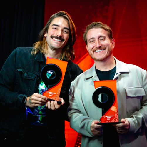 Representantes da Riot Games exibem troféus conquistados durante a gamescom latam awards 2026, destacando os prêmios recebidos por 2XKO e Wild Rift em um palco iluminado com tons vermelhos.
