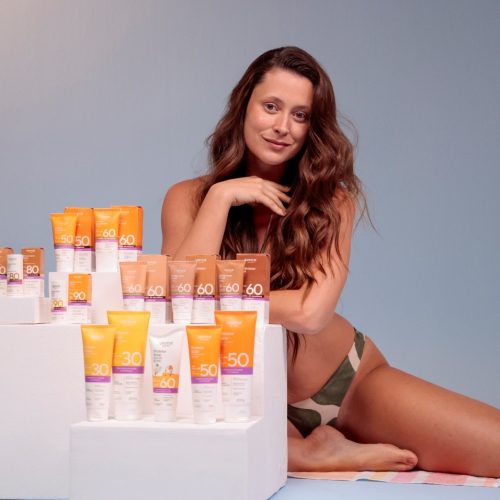 Modelo em estúdio ao lado da linha de protetores solares Labotrat Dermo Sun, com embalagens faciais e corporais expostas, destacando proteção solar e skincare.