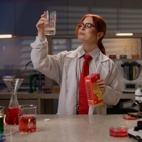 Cientista em laboratório analisa bebida vegetal Possible, segurando embalagem de achocolatado enquanto observa amostras coloridas em um cenário científico.