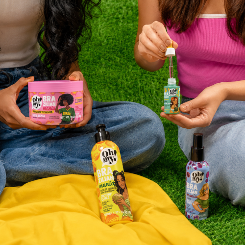 Produtos da Oh My! Brazil da linha Brazilian Mania aparecem em um piquenique ao ar livre, com duas mulheres utilizando os finalizadores capilares, reforçando a proposta de cuidado, leveza e beleza inspirada no Brasil.