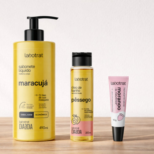Produtos Labotrat dispostos sobre mesa de madeira com fundo branco, incluindo sabonete líquido Labotrat Maracujá 490ml com pump preto, óleo de banho Labotrat Pêssego 200ml em frasco transparente e hidratante labial Labotrat Morango 10g em bisnaga rosa e branca, embalagens originais preservadas e alinhadas em composição minimalista.