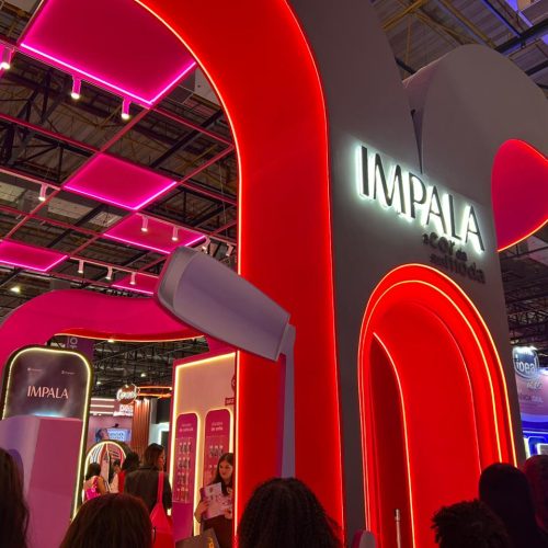 Estande da Impala na Beauty Show com iluminação rosa e vermelha, destacando a identidade visual da marca e o espaço dedicado aos lançamentos de esmaltes.