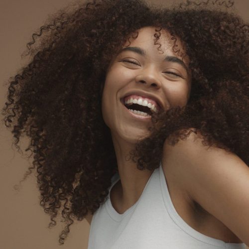 Mulher sorrindo com cabelos cacheados volumosos e naturais, representando a diversidade capilar valorizada pela Skala no hair care brasileiro.